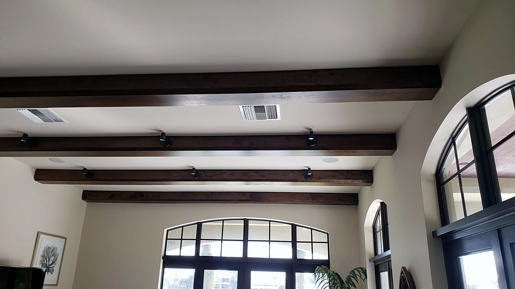 Living room with a stained beamed ceiling, arched steel-framed doors and a waterfront view