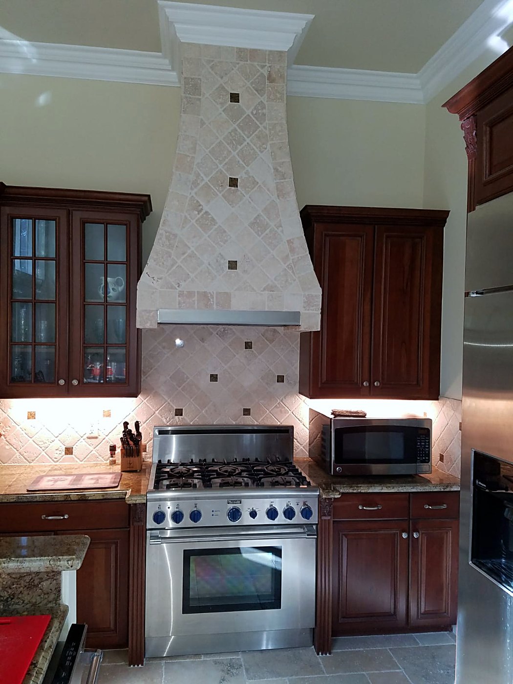 Kitchen with a stone range hood, travertine backsplash and cherry cabinetry