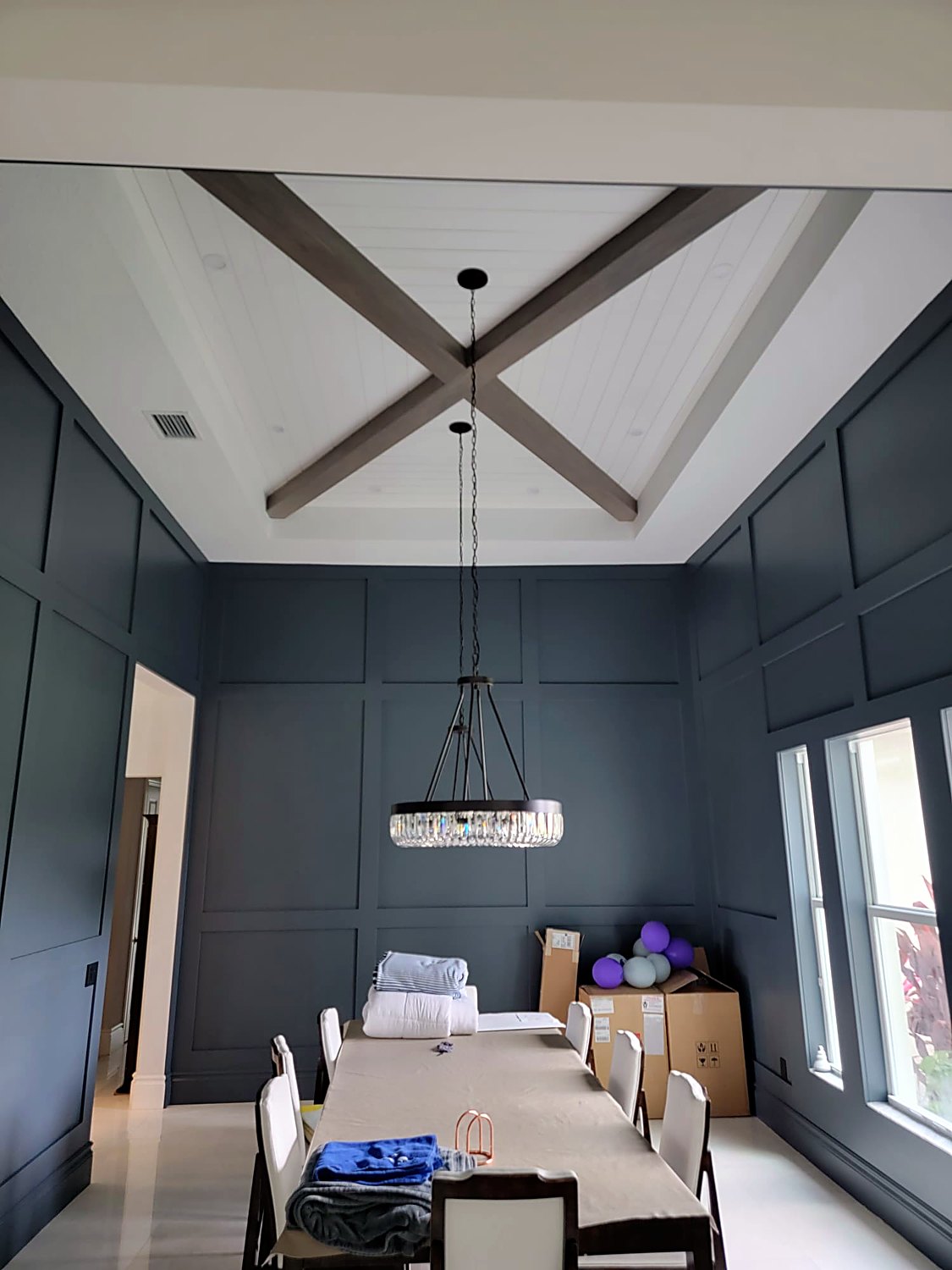 Navy panel-moulded dining room with an X-beam ceiling and chandelier