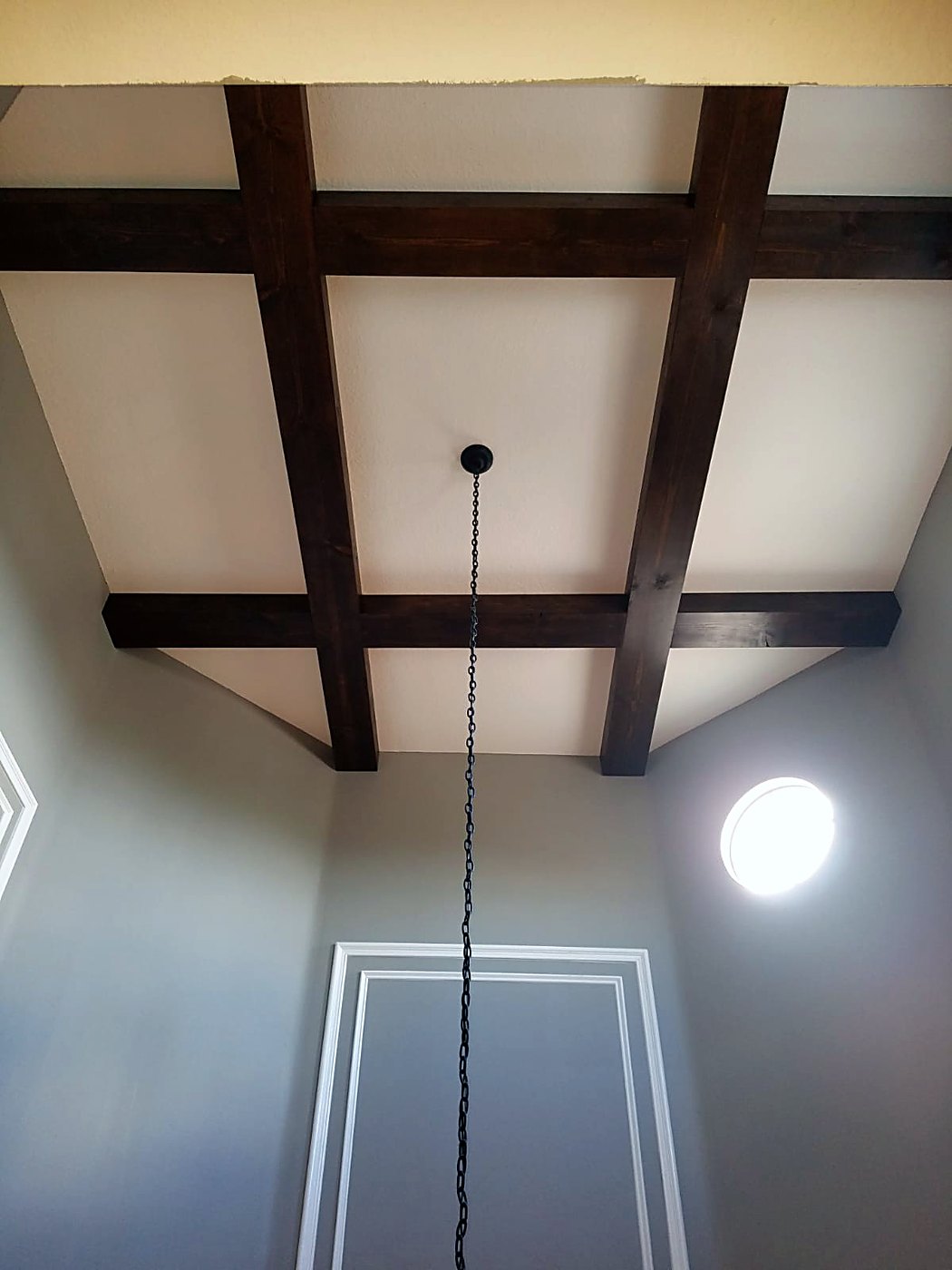Dark-stained ceiling beams in a double-height room with a round window